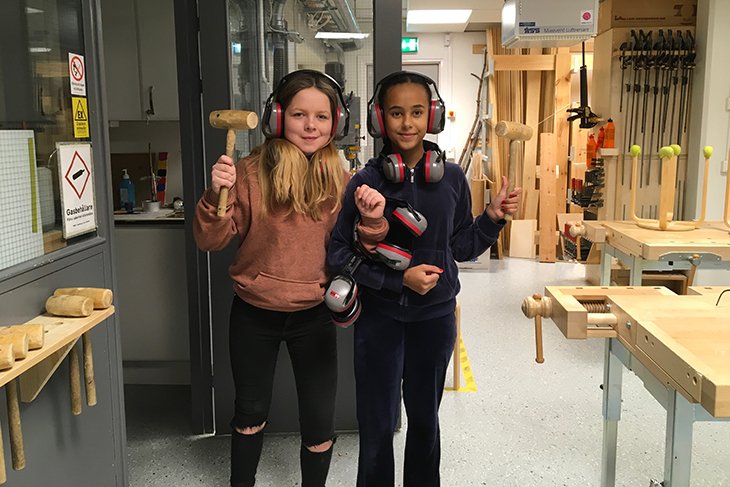 Två elever som står med verktyg i händerna och tittar in i kameran.